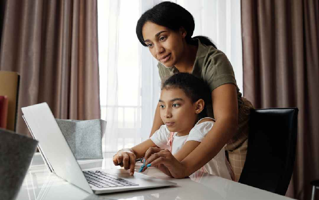 mother helping her daughter use a laptop
